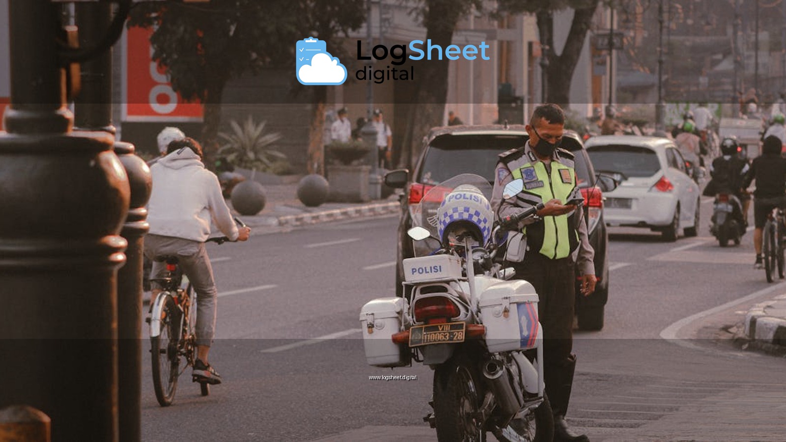 A police officer checks his phone near motorcycles on a busy city street with cyclists and cars.