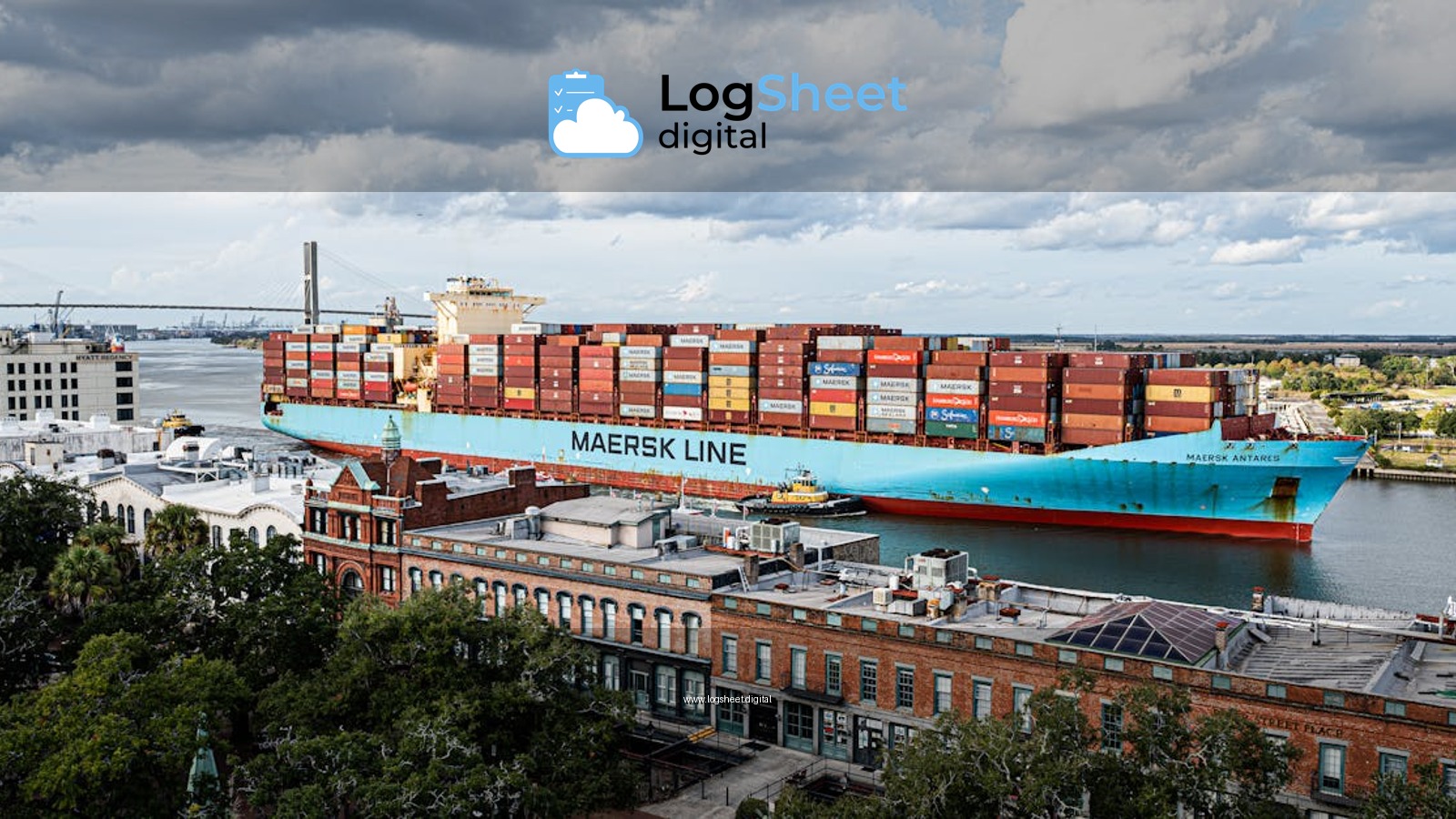 Aerial view of a cargo ship on the Savannah River with a city backdrop and cloudy sky.