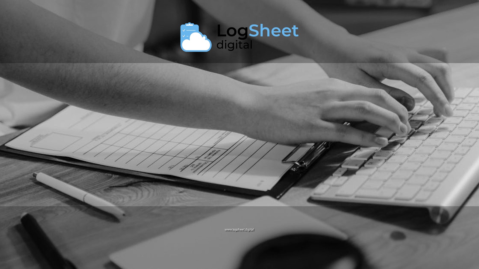 Black-and-white photo of hands typing on keyboard with clipboard on wooden desk.