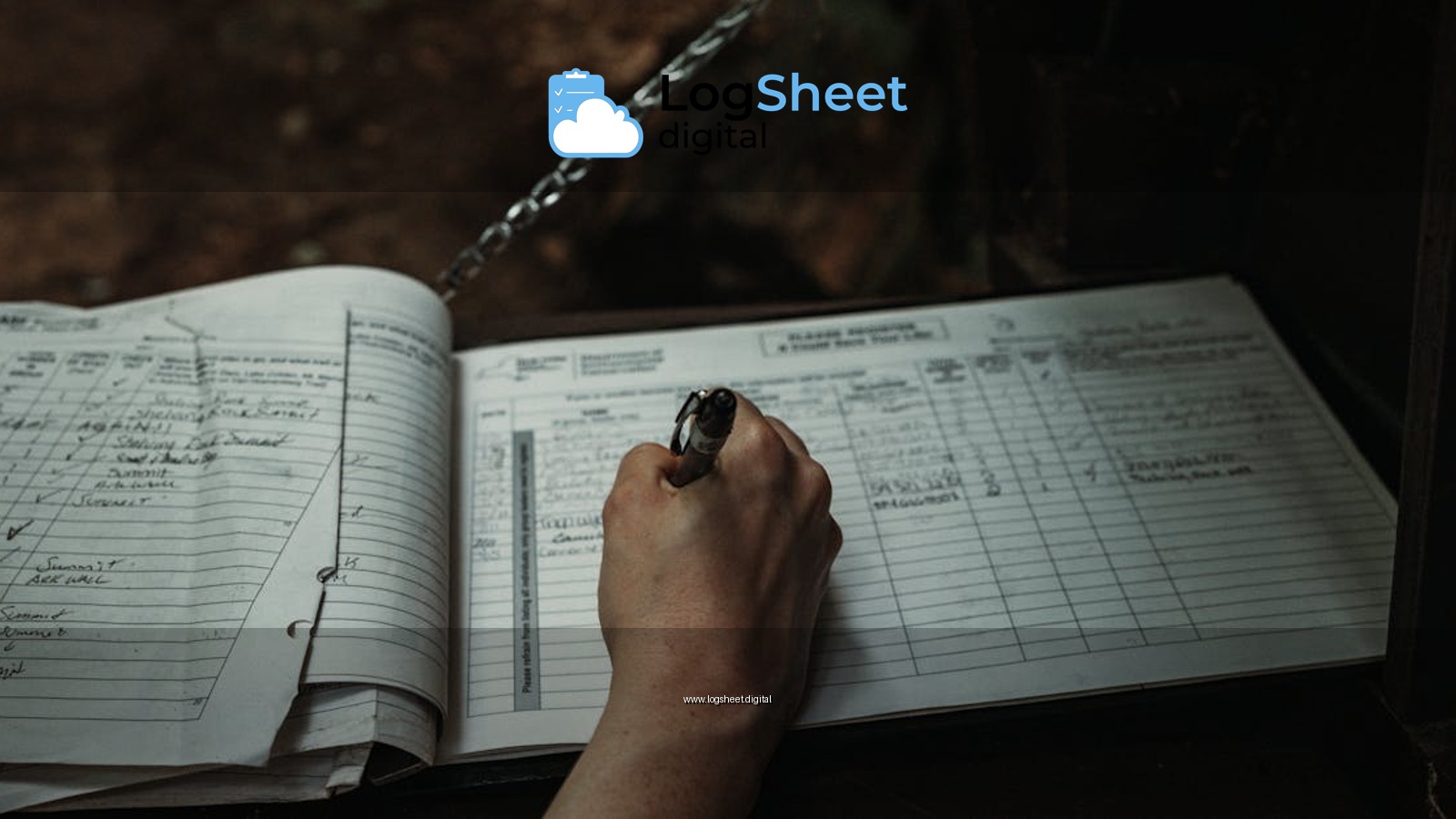 Close-up of a person writing in an outdoor logbook on a table.