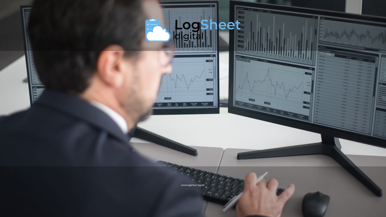 A businessman in a suit analyzing financial charts and graphs on two computer monitors indoors.