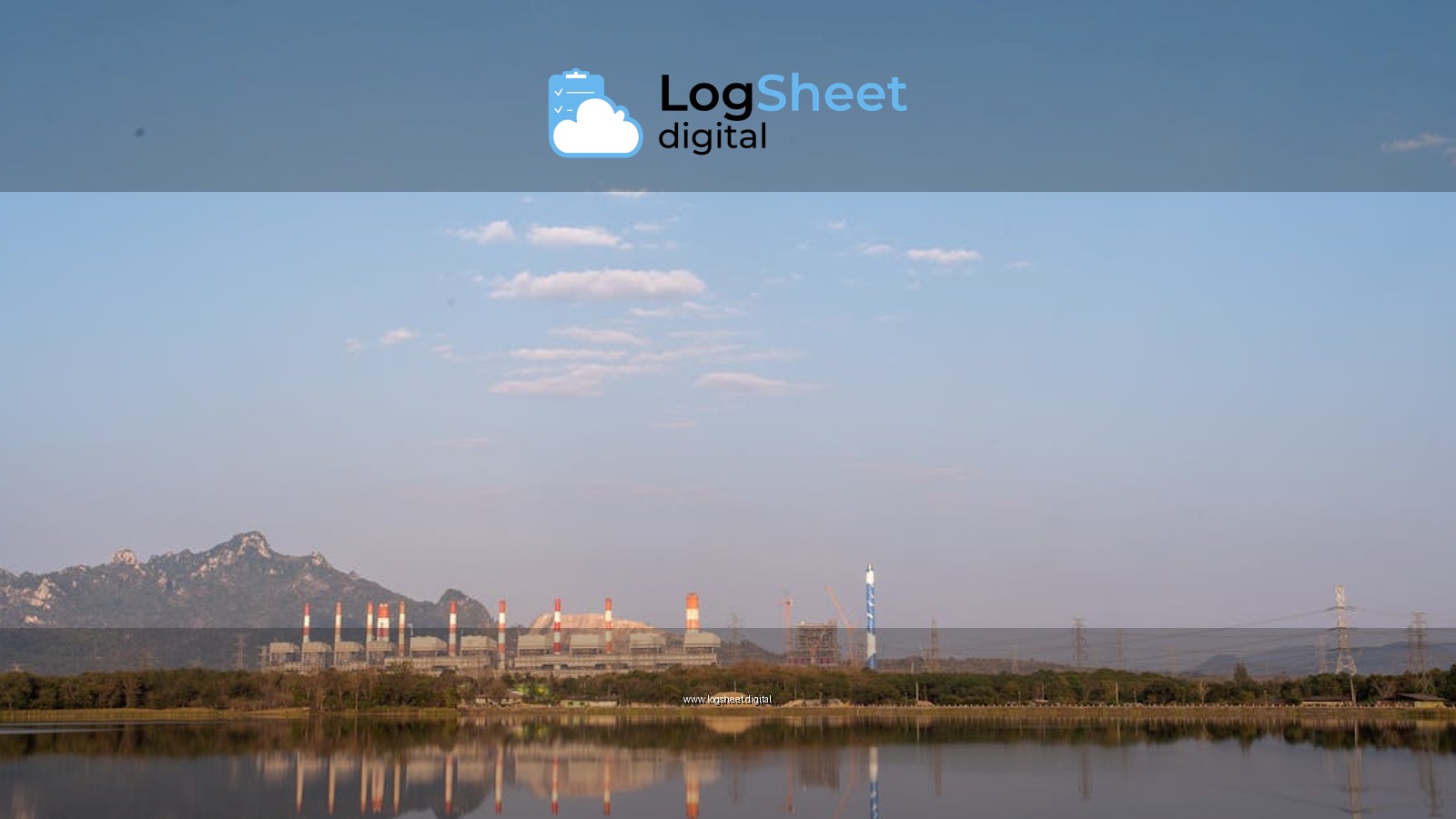 Scenic view of a power plant by a lake, reflecting mountains and a sky with scattered clouds.