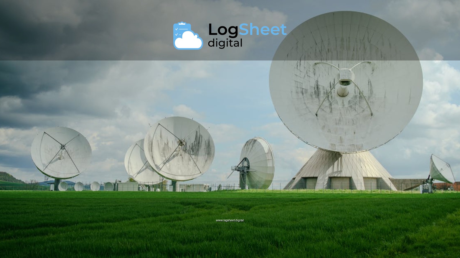 Array of large satellite dishes in a lush green field under a cloudy sky.