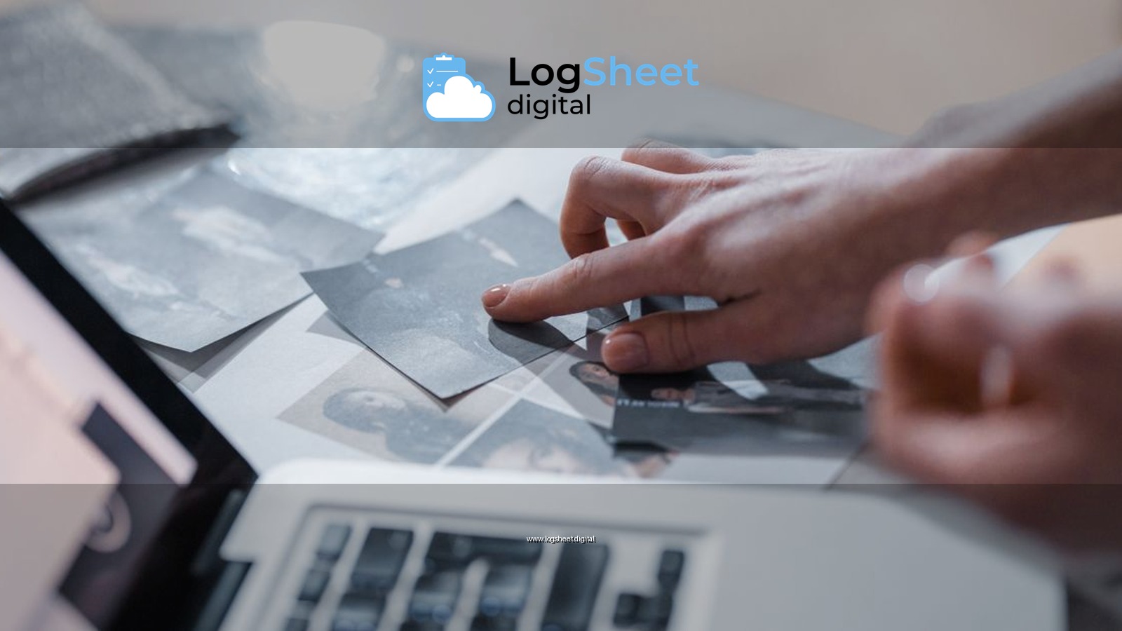 A hand arranges vintage photographs near a laptop in a modern workspace.